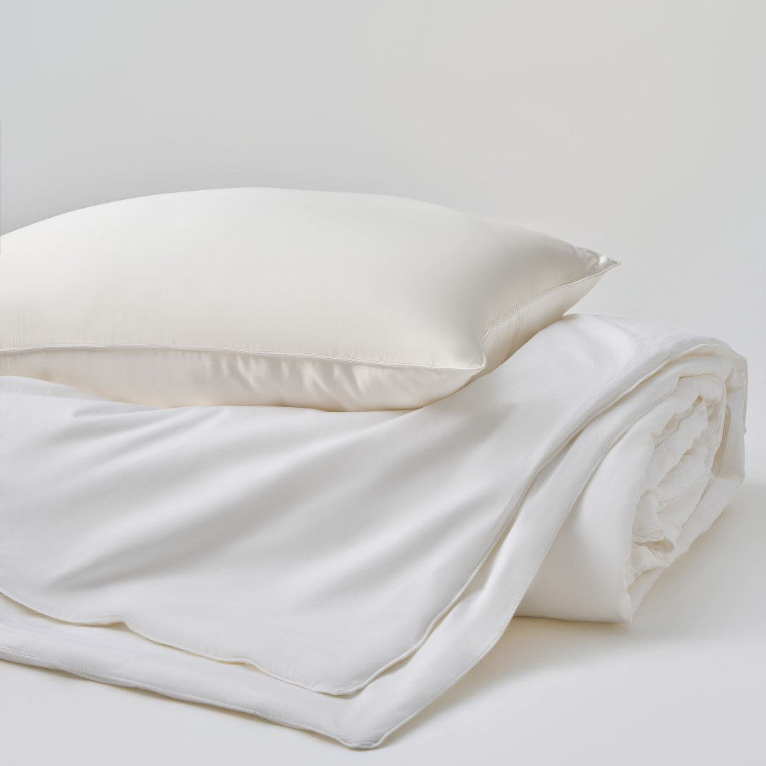 A luxury bedding bundle featuring a 100% Grade 6A Mulberry silk comforter stacked beneath a matching silk pillow in pearl white