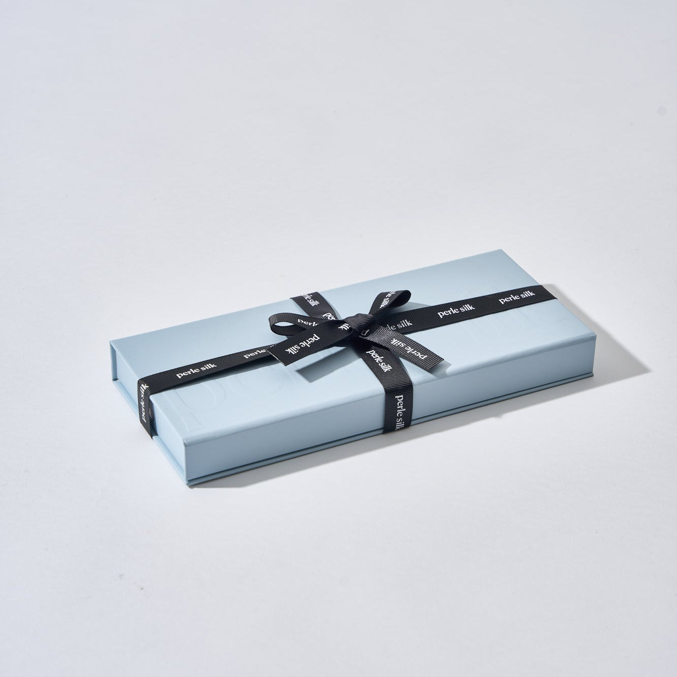 Gift box with a black ribbon on a light gray background perle silk