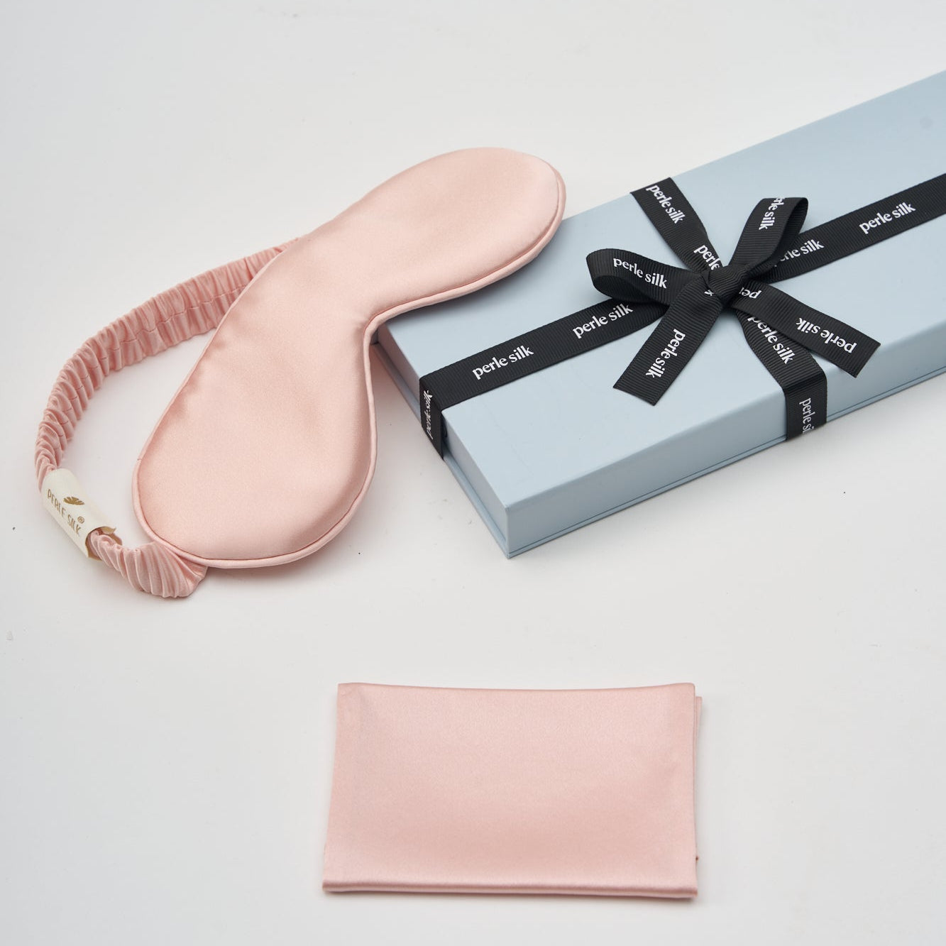 Pink sleep mask and pouch with a gift box on a light gray background