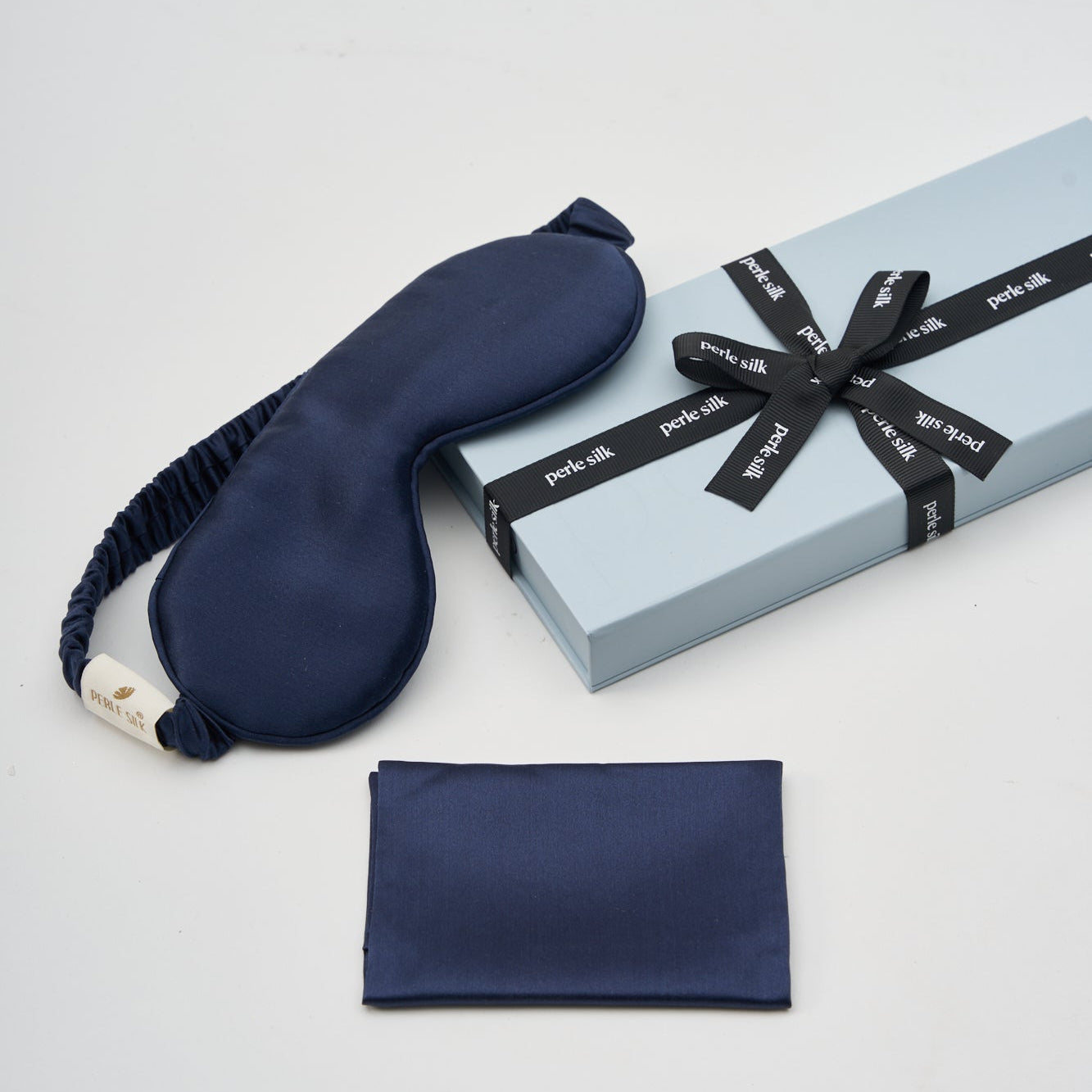 Navy sleep mask and pouch with a gift box on a light gray background